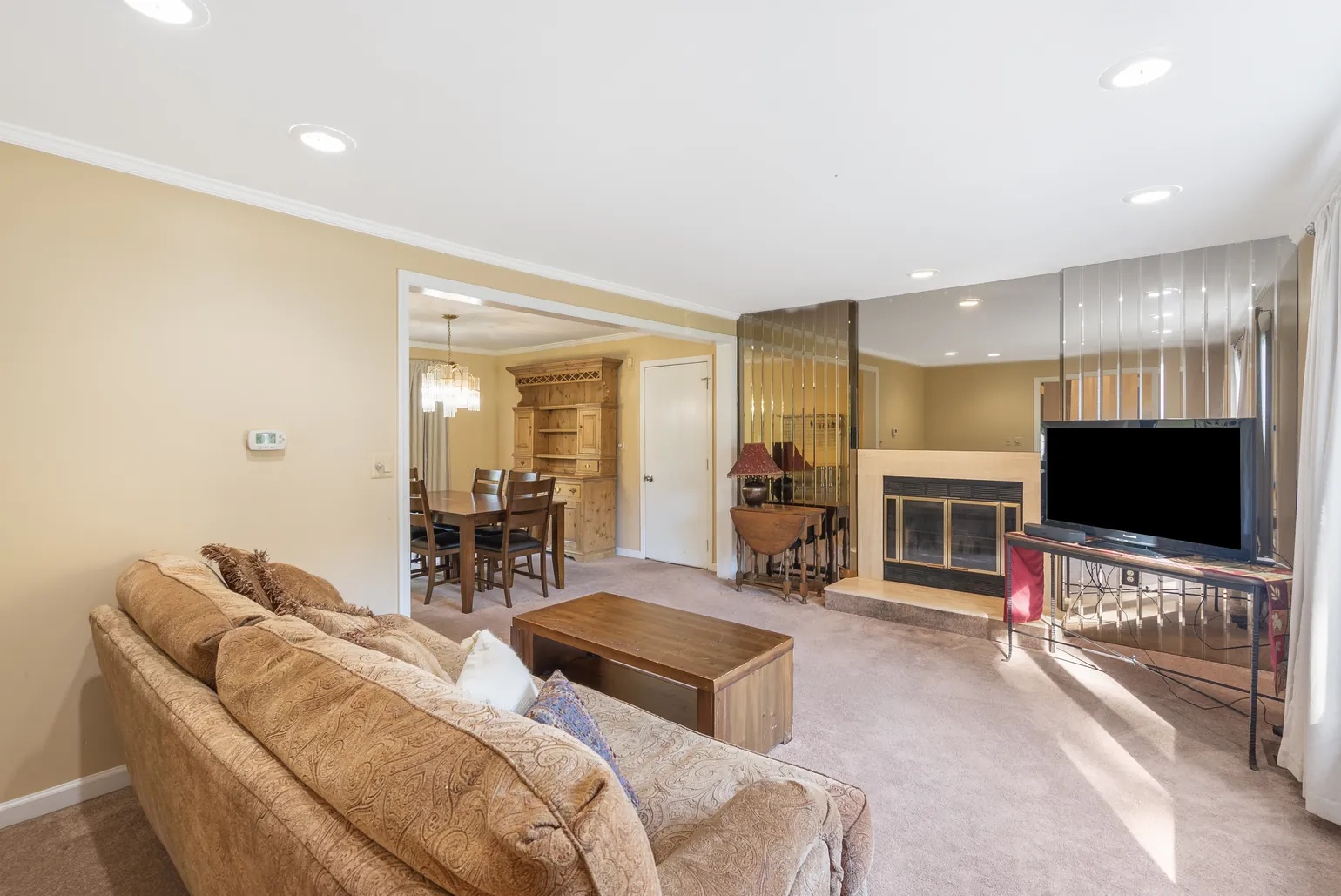 Living room with a paisley sofa and wood coffee table, a fireplace and television on a stand, and the dining room visible through the doorway